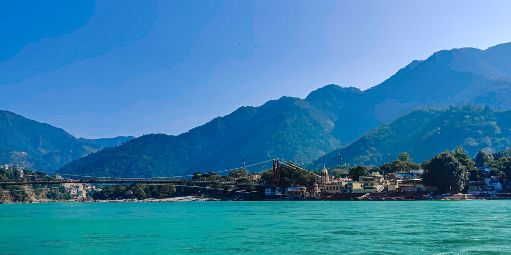 a scenic view of mountains behind a river in Rishikesh