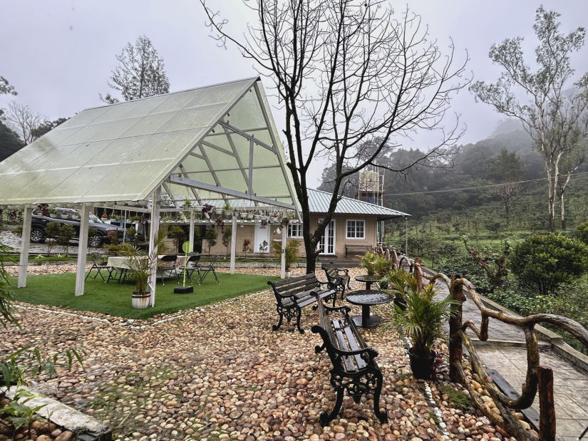 a glass house with seating arrangements below it next to fallen leaves - Ibex Stays & Trails, Valparai (Mistly)