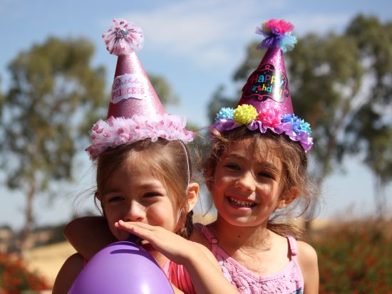 A child blowing a balloon while her friend and her pose for a picture