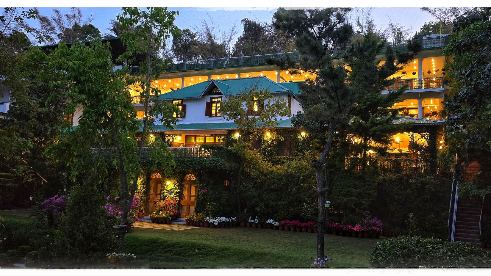 Twilight view of Shaheen Bagh-Dehradun, a luxury boutique resort and spa, with warm lights illuminating its green-trimmed architecture and lush gardens