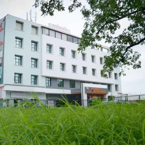  Lush green foreground framing the exterior view of Hotel Polo Max under a cloudy sky.