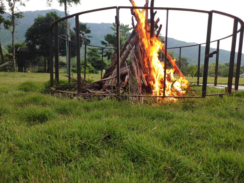 a bonfire inside metal casing area surrounded by green grass - Black Thunder, Coimbatore