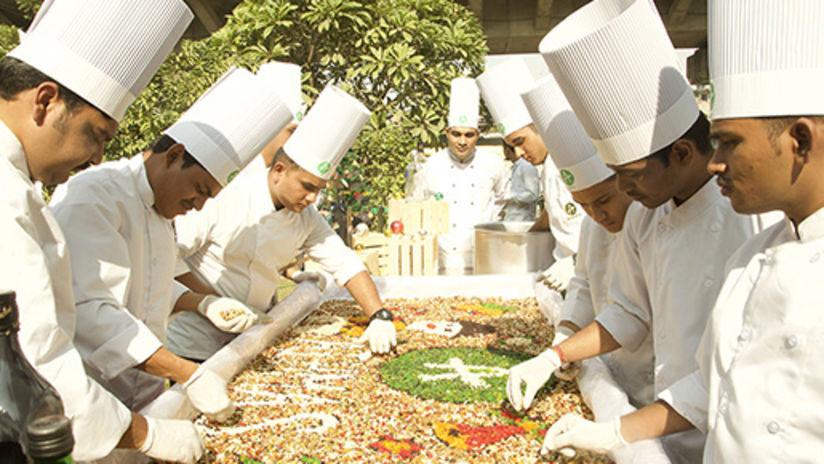 Our expert chefs gather around a table to carve our logo in food grains 