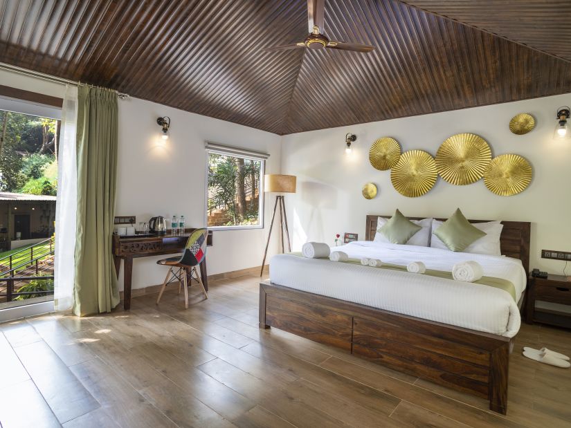 A hotel room with a large wooden bed and a door opening to the lush garden - Stone Wood Nature Resort, Gokarna