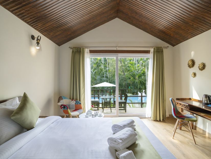 A view of a hotel room with comfortable bed, furniture and a balcony opening up to the pool - Stone Wood Nature Resort, Gokarna