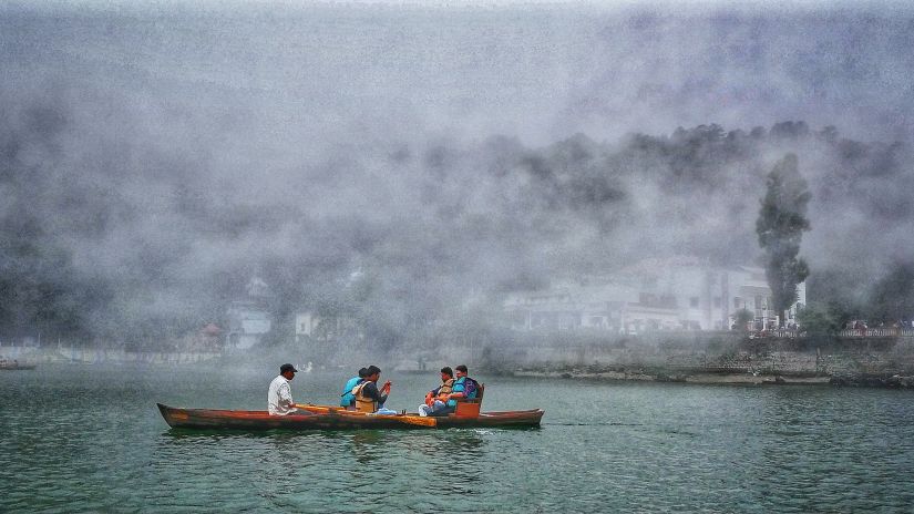 Five individuals rowing a boat in the centre of a lake on a cloudy day