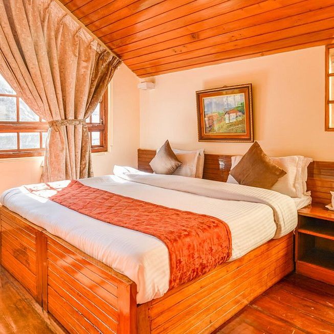 A suite room, featuring a spacious bed positioned adjacent to expansive windows adorned with curtains, while mirrors adorn another side at Sumitel Oriental, Gangtok.