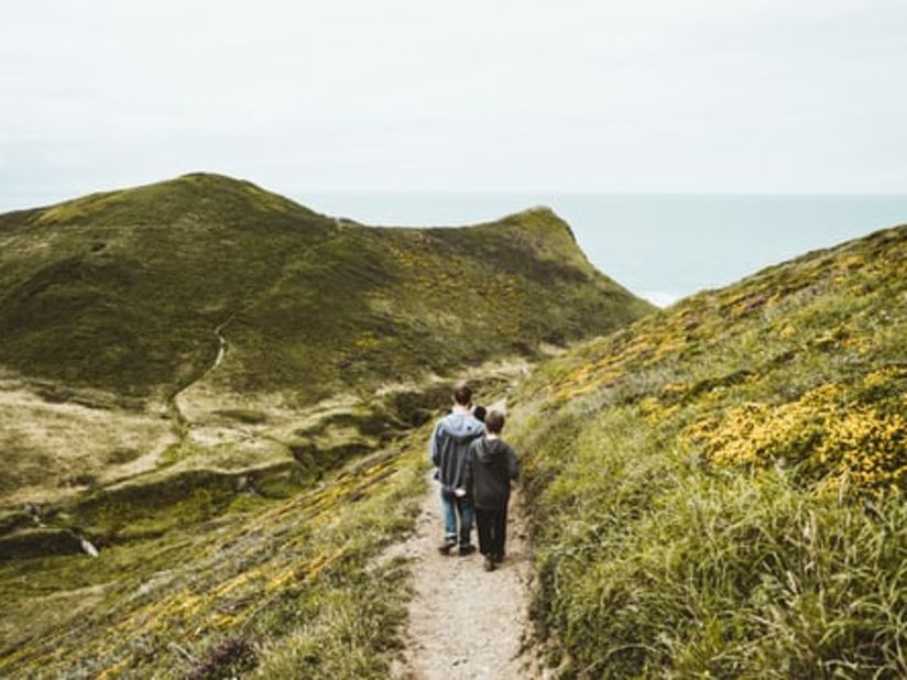 people walking on a a road between grass covered mountains