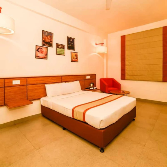 alt-text A hotel room featuring a single bed with a large mural of a cityscape, a working area with an ergonomic chair, and a warm color scheme.