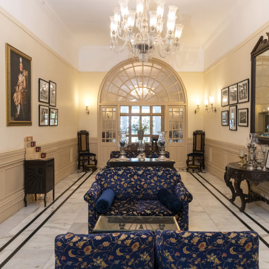 alt-text The lobby in The Claridges Nabha Residence, Mussoorie, contains sofas, paintings, a chandelier, a mirror, and various decor items.