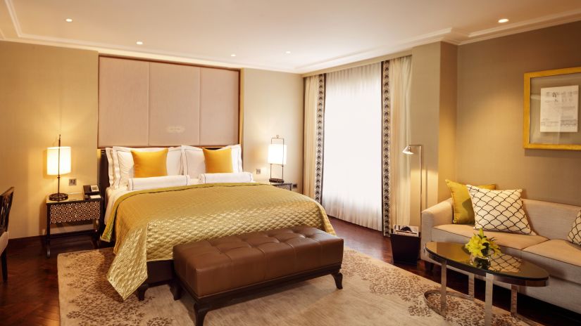 Front side view of a bedroom with a bed with golden covers and sofas for sitting - The Claridges, New Delhi 