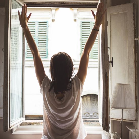 A person is standing in front of open window and stretching hands. 