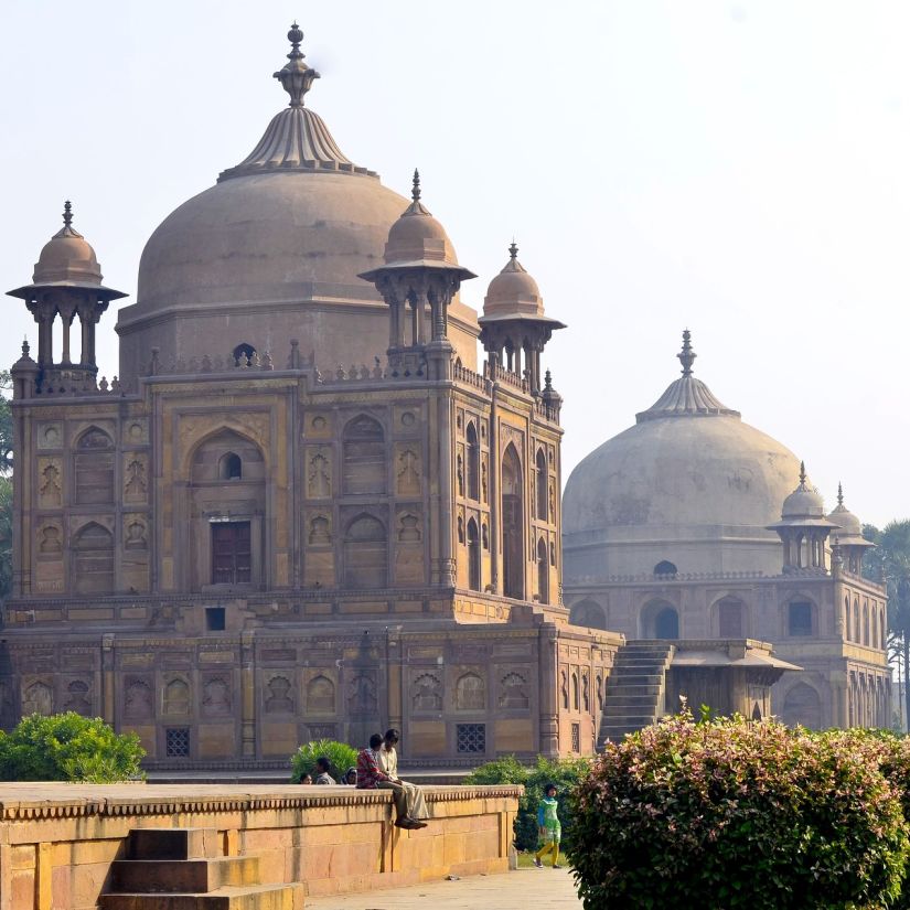 A domed sandstone mausoleum in a garden setting under a clear sky.