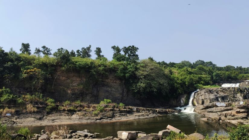 an overview of a waterfall cascading down to a waterbody with forest cover in the background