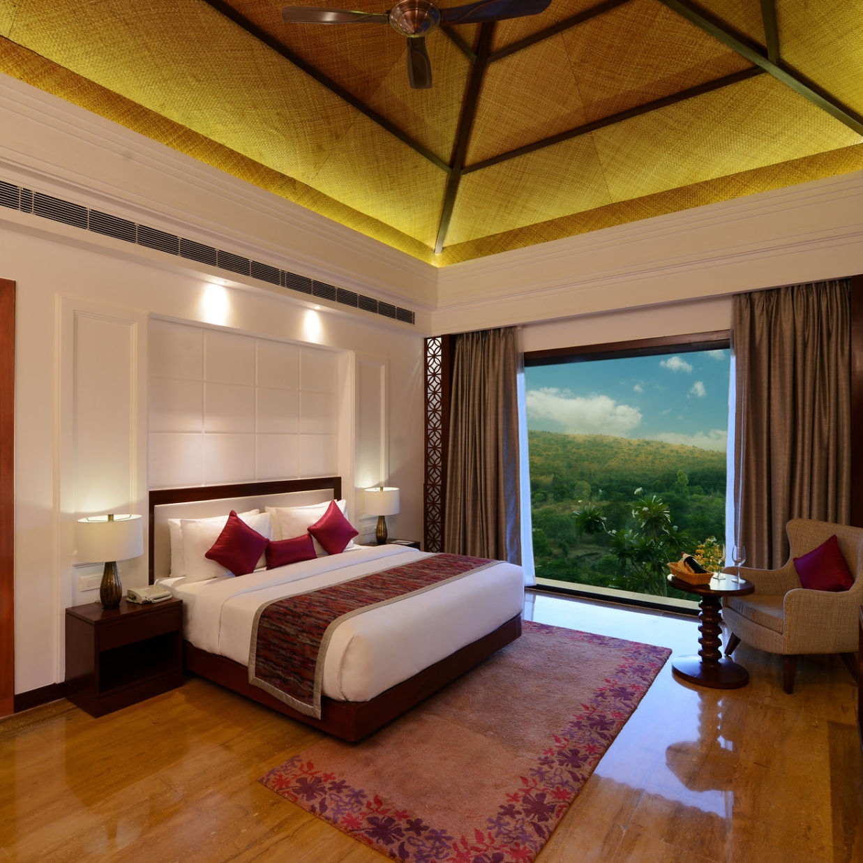 A king size bed with side tables, a floor to wall window, and door leading to the bathroom inside the executive suite - The Ananta Udaipur