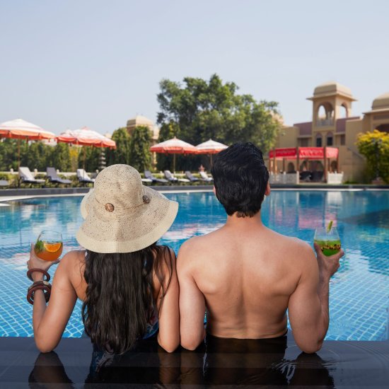 A couple unwinding in the pool, savoring drinks at HERITAGE VILLAGE RESORTS & SPA, MANESAR.