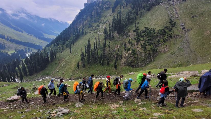 A group of trekkers climbing a mountain with other mountains covered by greenery in the background