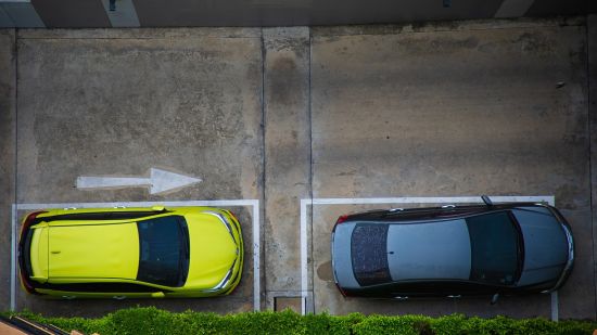 Two cars parked in a parking area and a sign of direction.