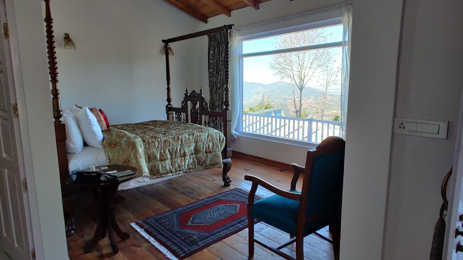  Side view of Superior Room  with bed and rug on the side and a chair by the wall at Te Aroha by Shervani Mukteshwar