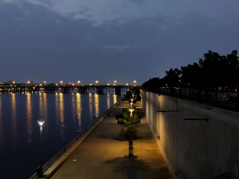 Serene view of river with city lights reflecting on it and a pavel way on one side for people to comfortably walk over it