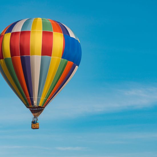 a solitary hot air balloon soaring in the sky with white clouds in the blue sky visible