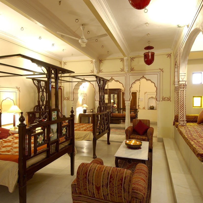 a brightly lit room with a two large beds with a canopy and sofas for sitting - Hotel Castle Mandawa, Jhunjunu