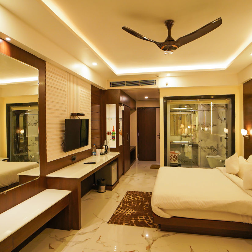 a double bed with a tv opposite to it wall mounted and a ceiling fan inside one of the rooms - Shanti Seaview Resort & Spa