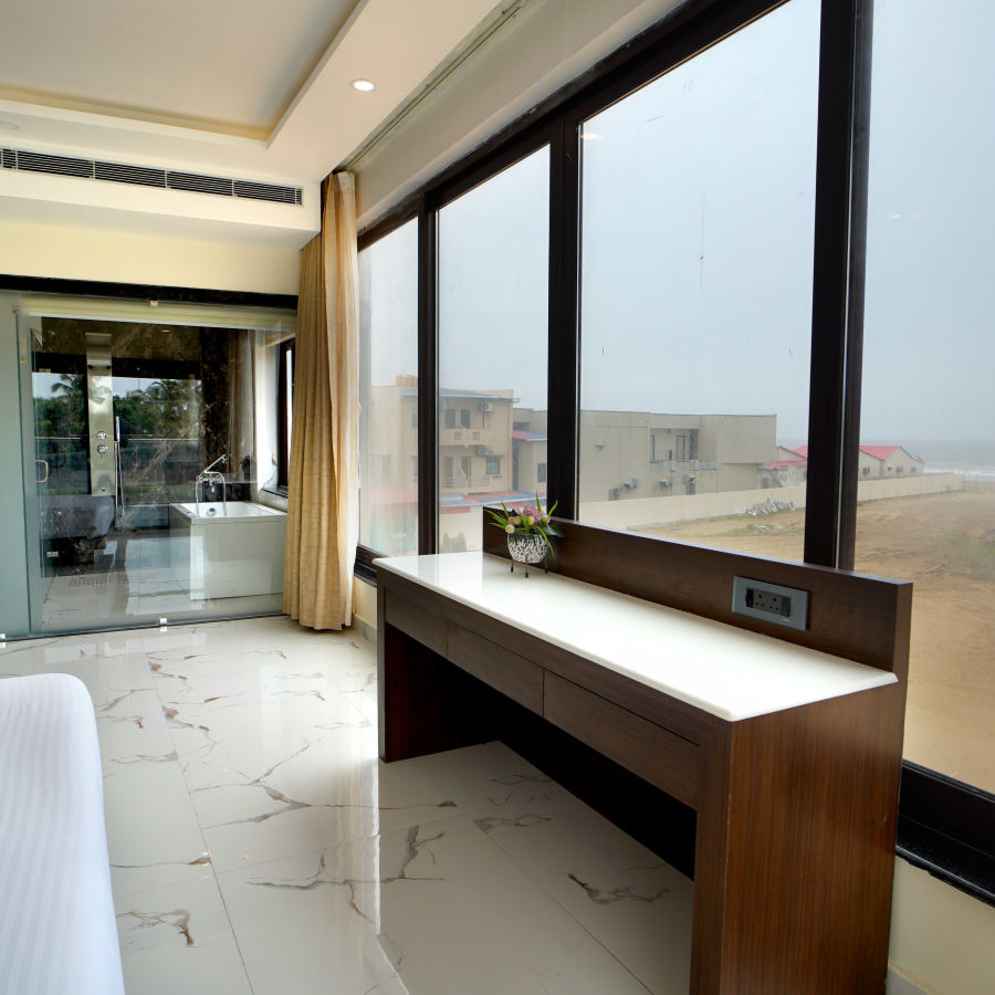 a table in front of floor to ceiling windows and a double bed opposite to it inside one of the rooms - Shanti Seaview Resort & Spa