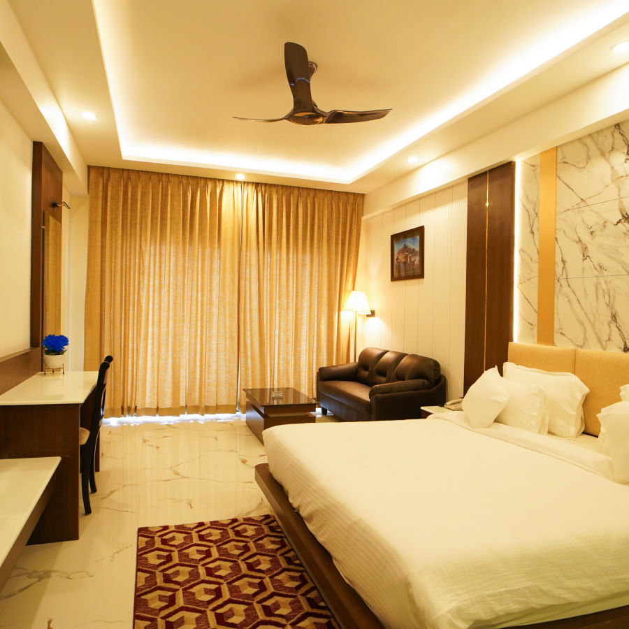 a double bed with a sofa on one side and a tv wall mounted opposite the bed in one of the rooms - Shanti Seaview Resort & Spa