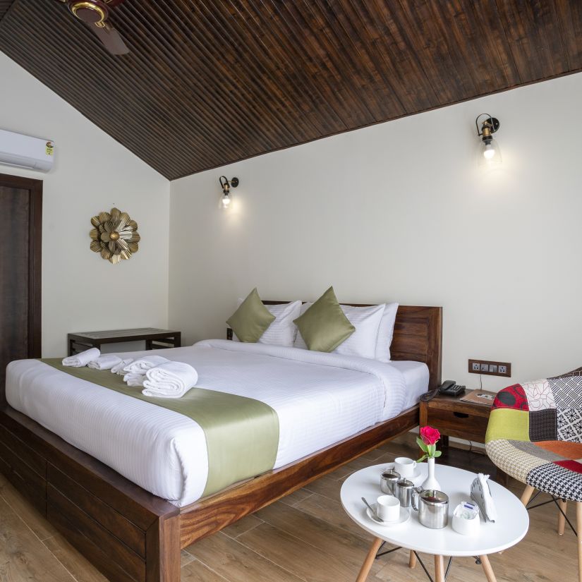 A hotel bedroom with a large bed with a green runner, hanging lamps and a chair placed in front of a coffee table - Stone Wood Nature Resort, Gokarna