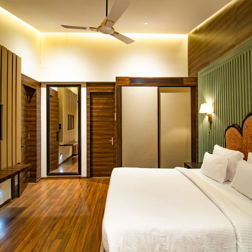 A side-view of the Villa Room shows a large bed, wooden panels on walls and a LED TV - Wedlock Greens Hotel Resorts Dhanbad