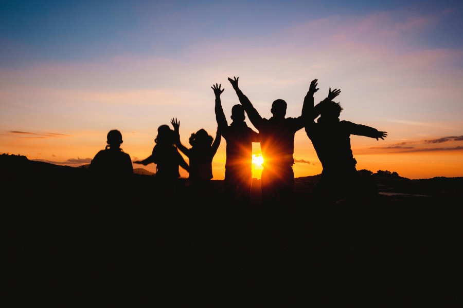 alt-text Silhouette of a group of people with raised arms, celebrating or posing against a vibrant sunset, creating a joyful atmosphere against a colorful sky.