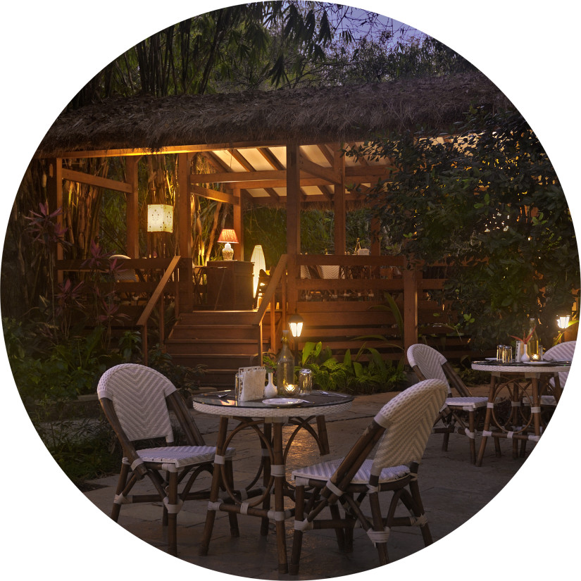 Night view of an outdoor dining area with chairs around tables and a cabin in the background.