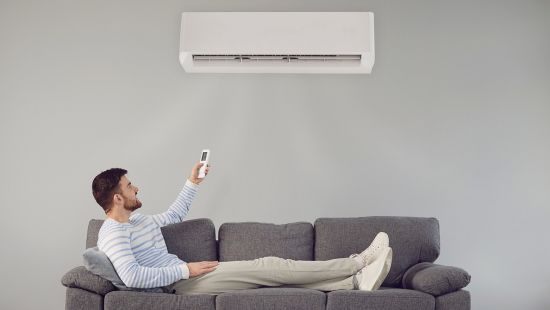 A man relaxes on a sofa as he uses the AC remote