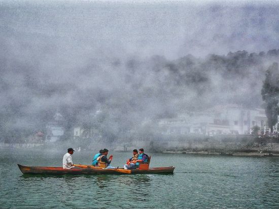 Five individuals rowing a boat in the centre of a lake on a cloudy day