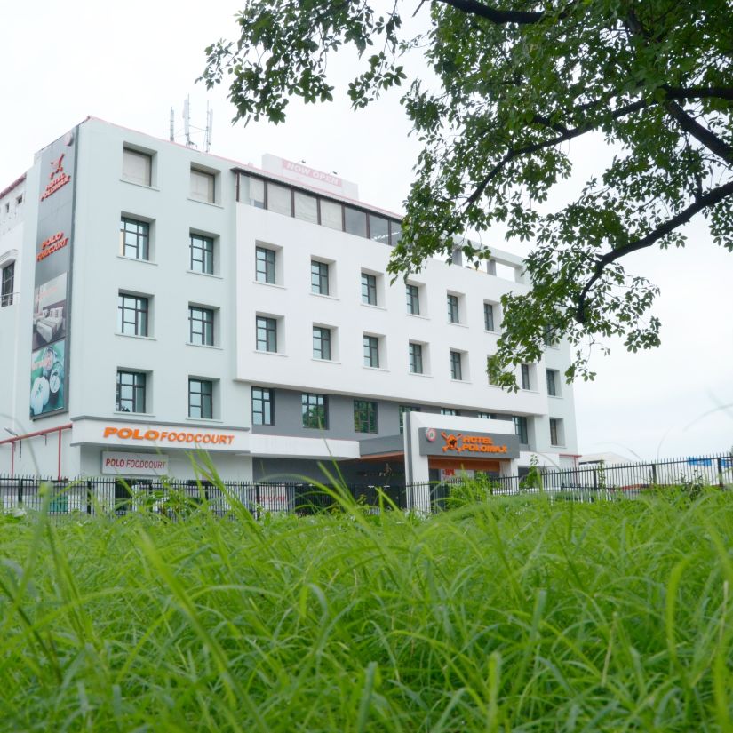 Hotel's facade  viewed from behind vibrant green foliage | Max Hotel Prayagraj.