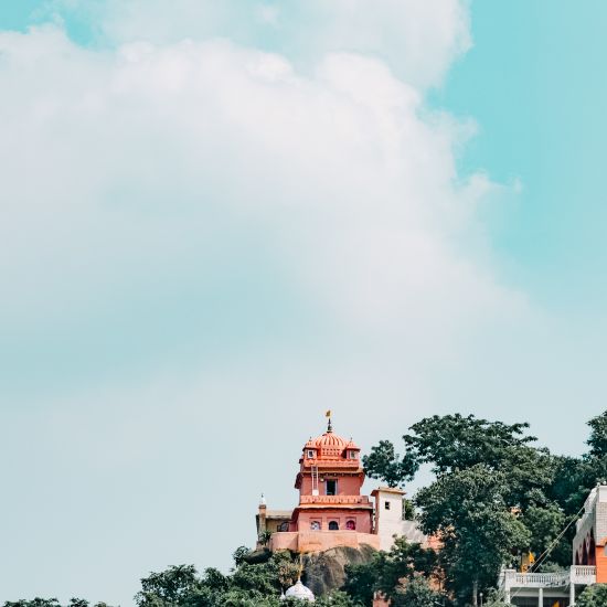 A hilltop temple with domes and spires, brightly colored against a cloudy sky.