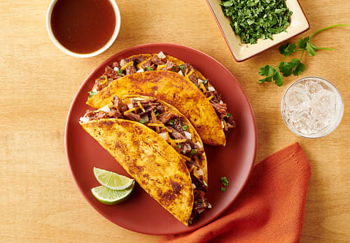 Serve tacos with seasoned broth: a plate featuring two tacos accompanied by a small bowl of salsa for dipping.