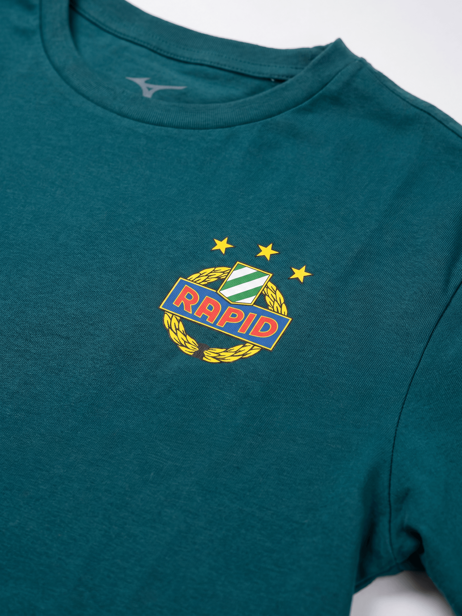 Rapid-Wappen mit drei Sternen und Mizuno-Logo auf petrolfarbenem T-Shirt.