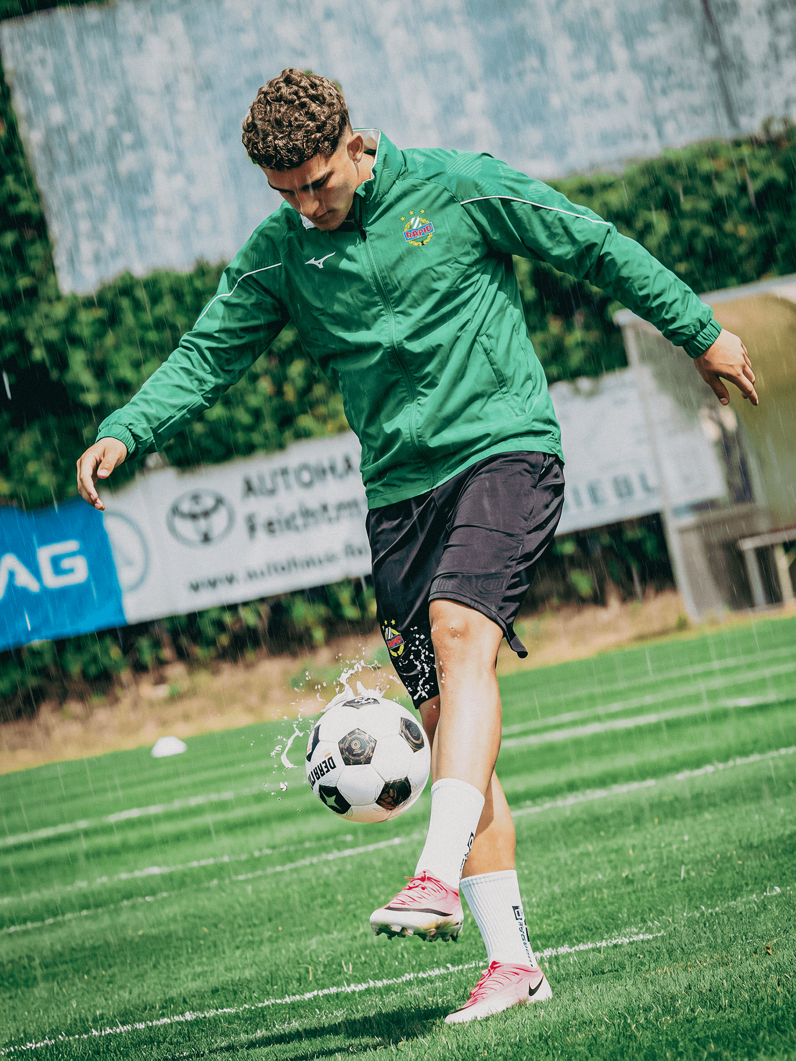 Spieler trägt die grüne SK Rapid Mizuno Regenjacke beim Fußballtraining im Regen.