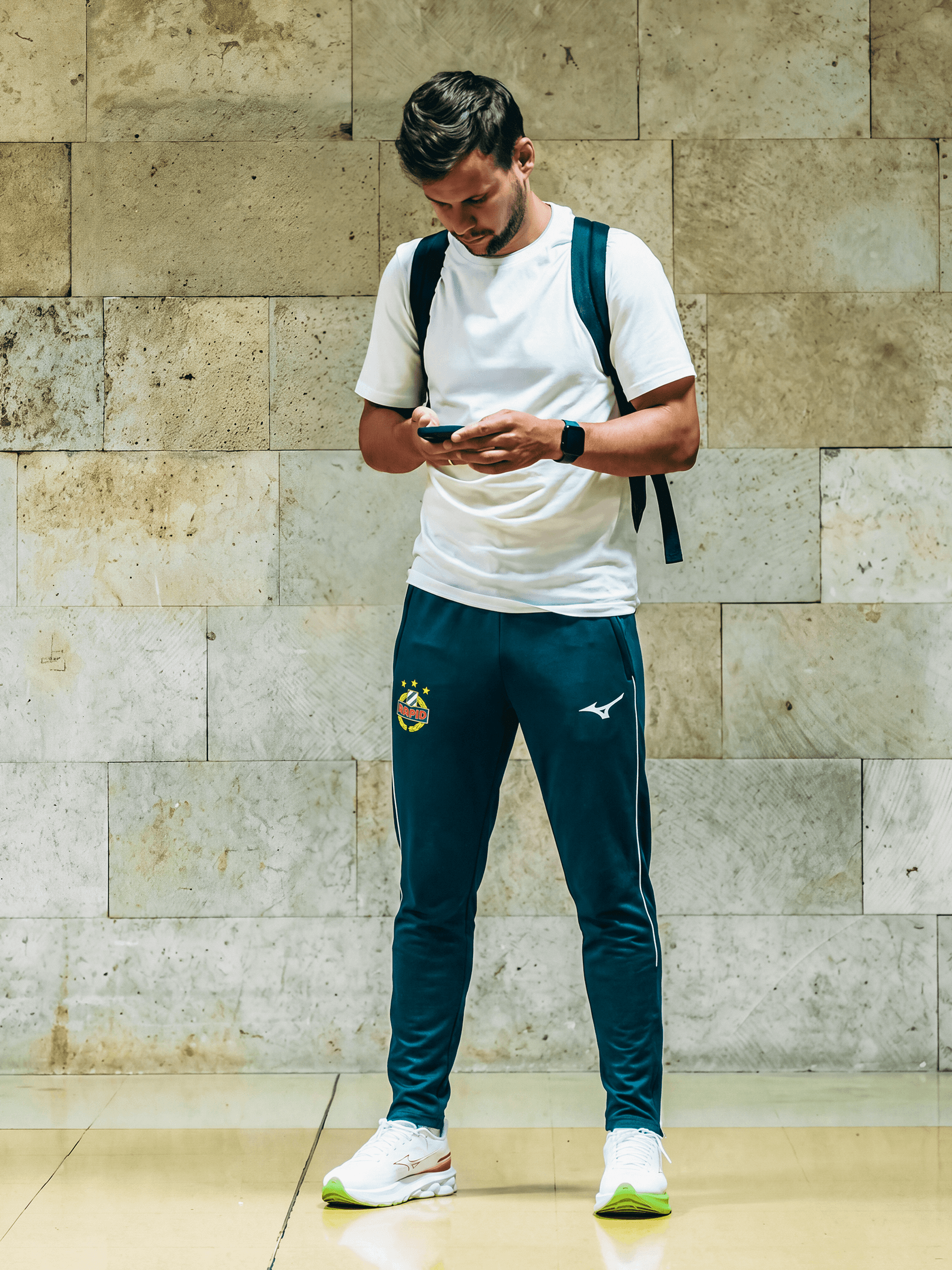 Person trägt die dunkelgrüne SK Rapid Mizuno Trainingshose im Alltag.