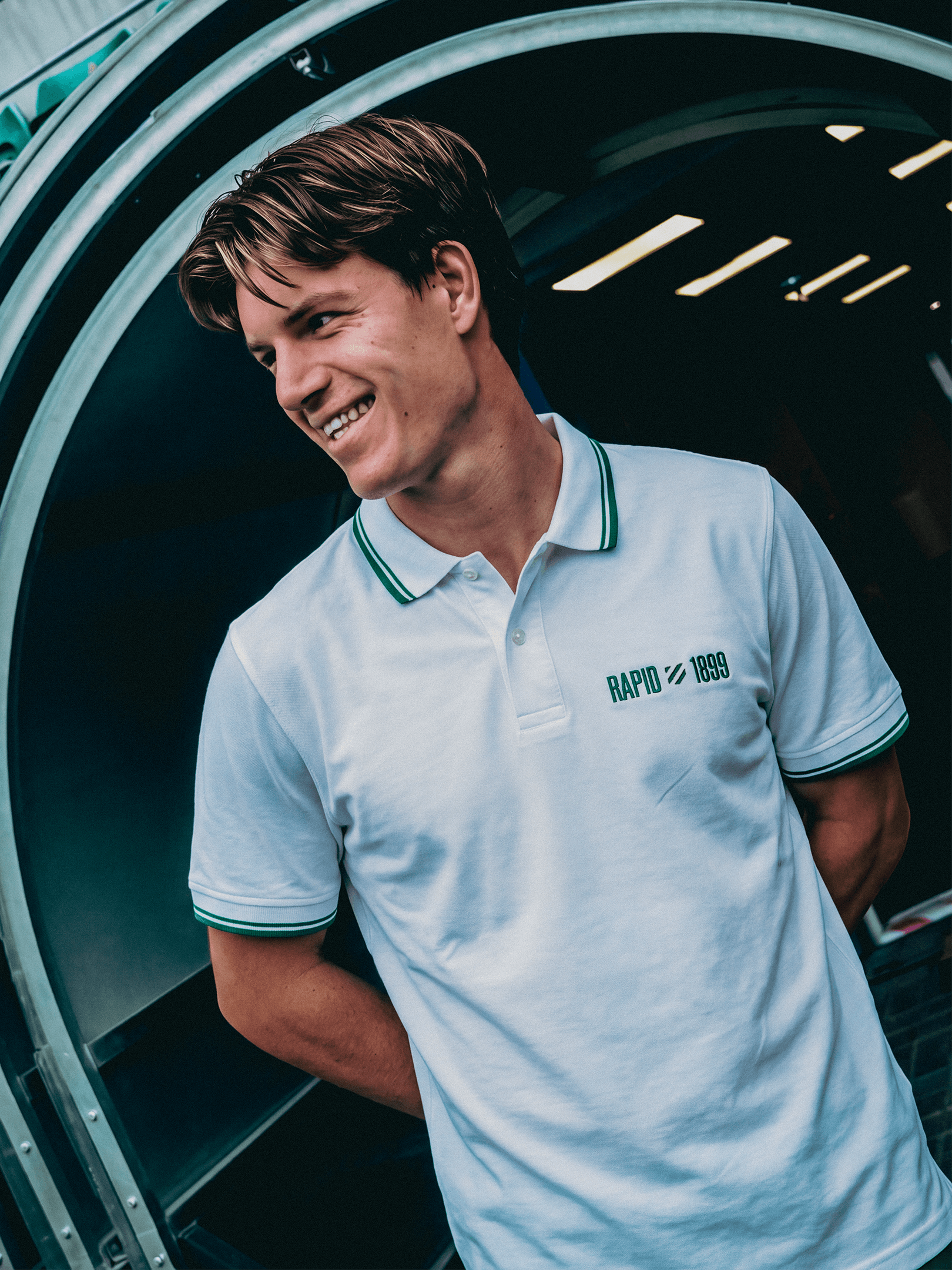 Person trägt das weiße SK Rapid Poloshirt Rapid 1899 mit grünen Details.