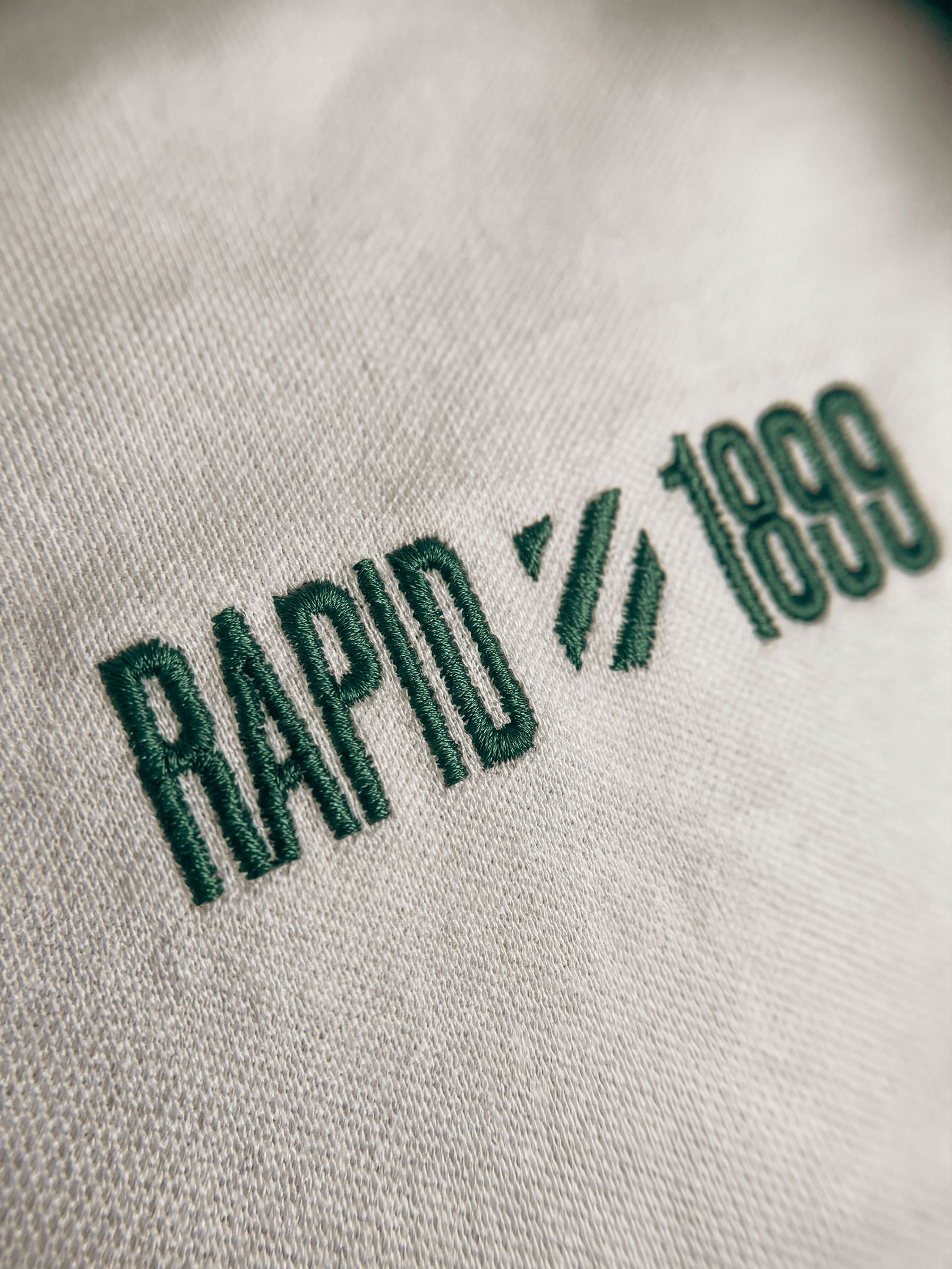 Nahaufnahme der grünen RAPID 1899 Stickerei auf dem weißen Poloshirt.