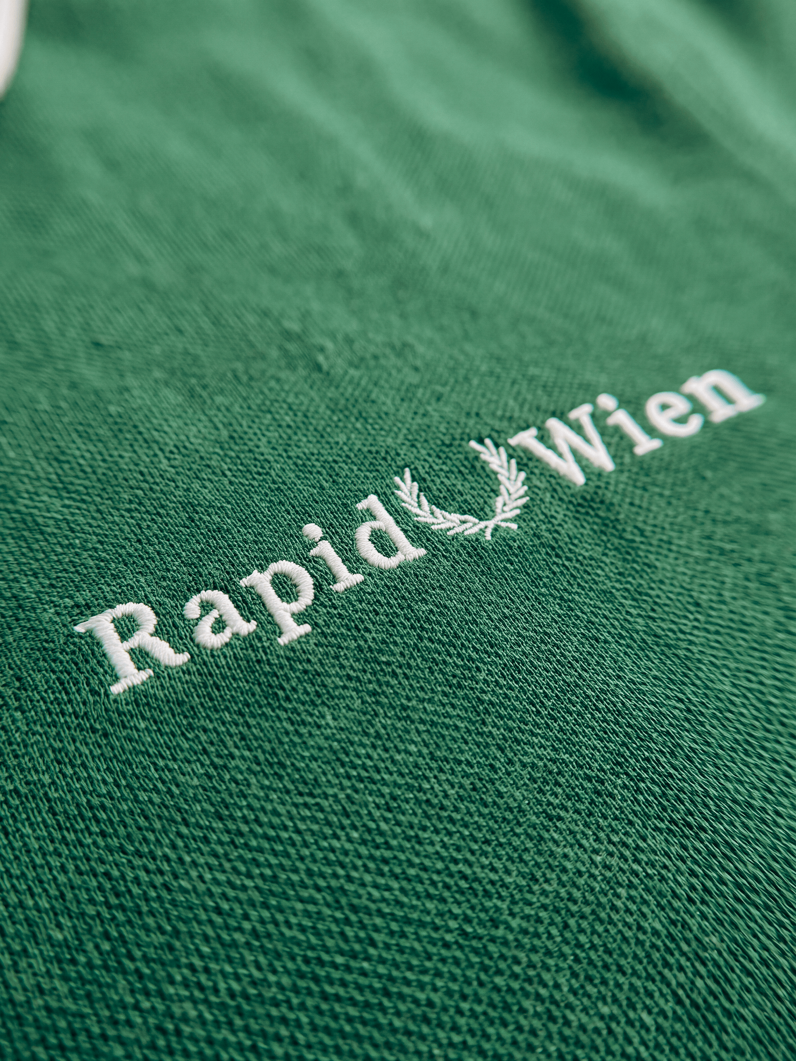 Nahaufnahme der Rapid Wien Lorbeer-Stickerei auf dem grünen Poloshirt.