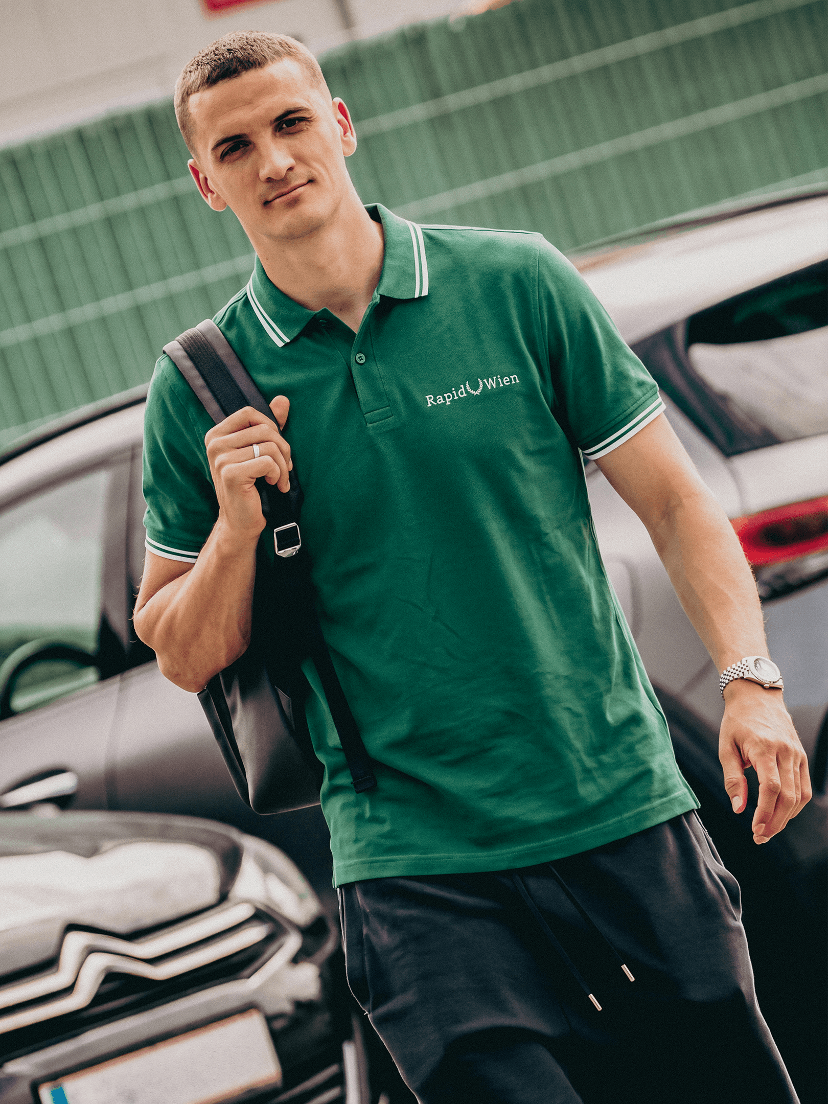 Person trägt das grüne SK Rapid Poloshirt Lorbeer mit weißer Stickerei.