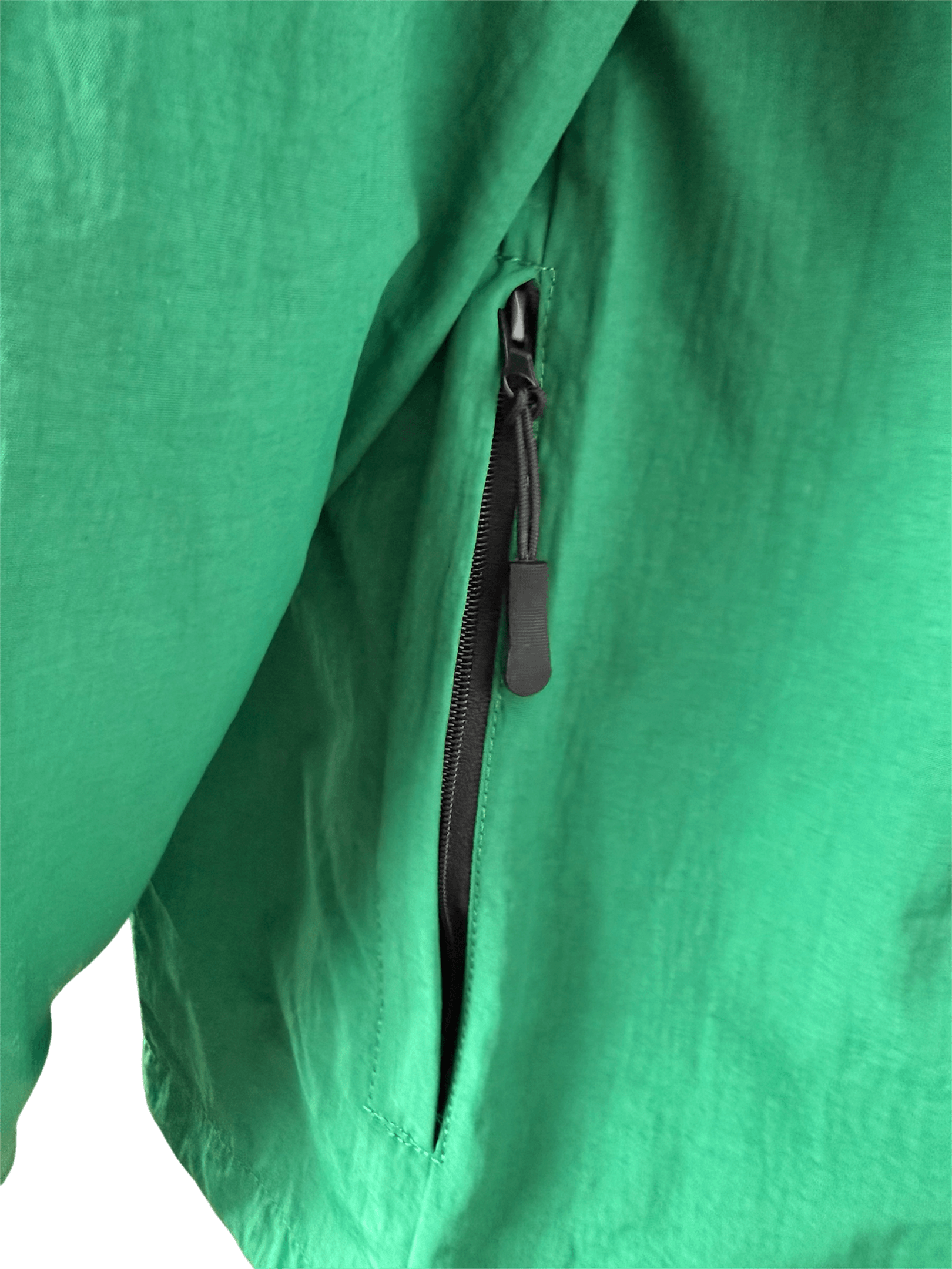 Seitliche Reißverschlusstasche am grünen Windbreaker Wappenschild.