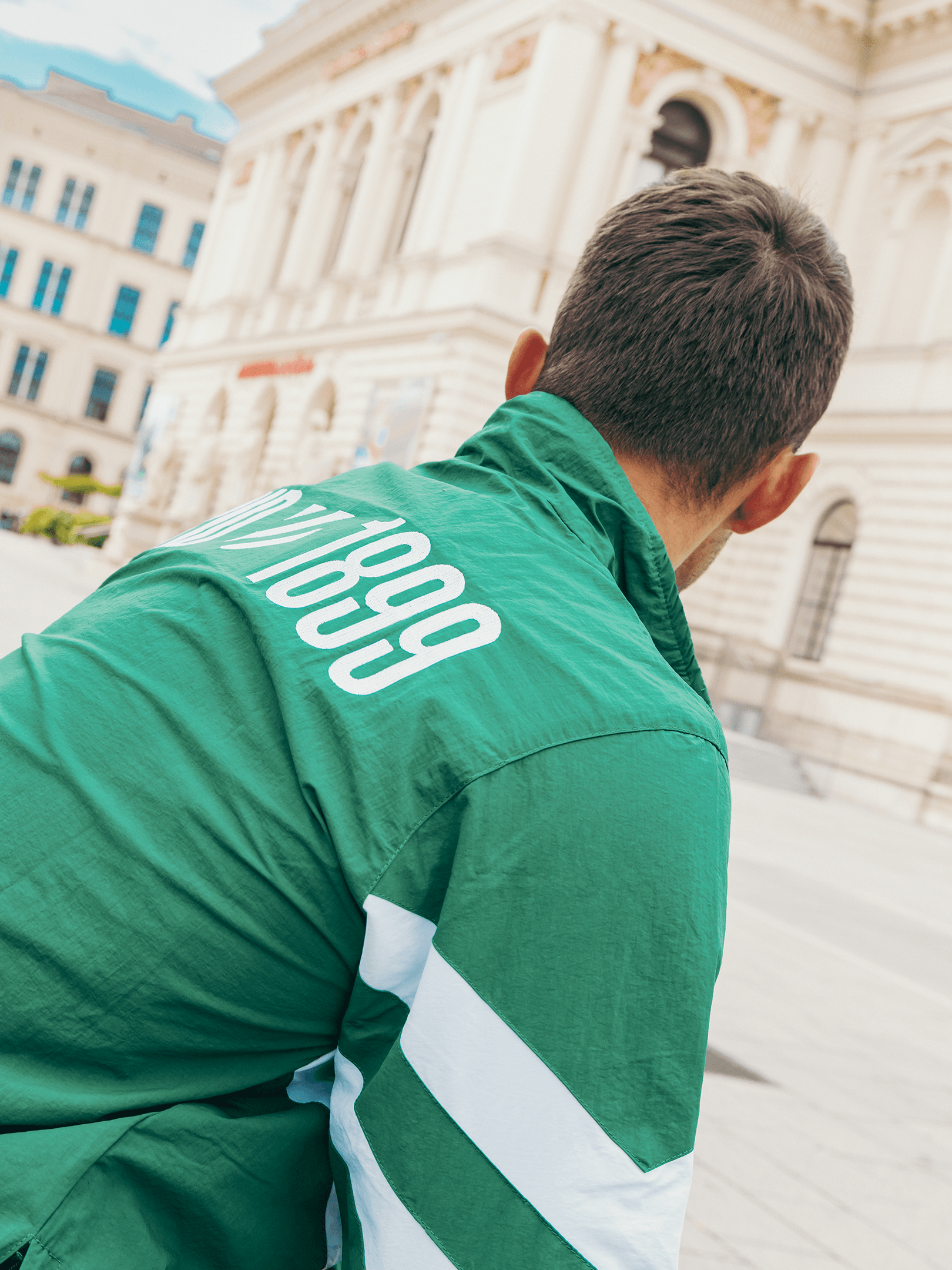 Rückseite des grünen SK Rapid Windbreakers mit weißem 1899-Schriftzug und Ärmelstreifen.