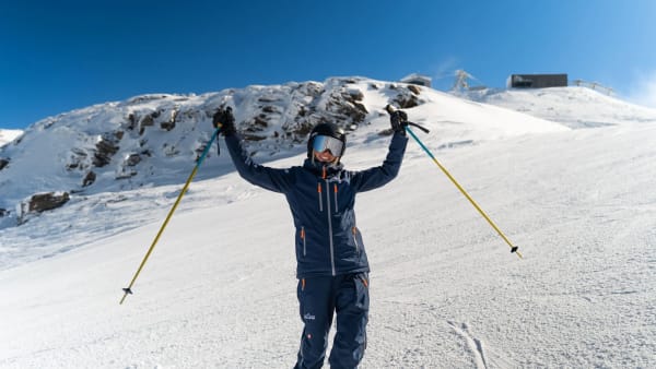 Glad Skilink-skiguide p� pisten med bl� himmel og arme i vejret