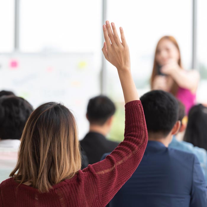 Woman raising hand with a question while other woman points at her.