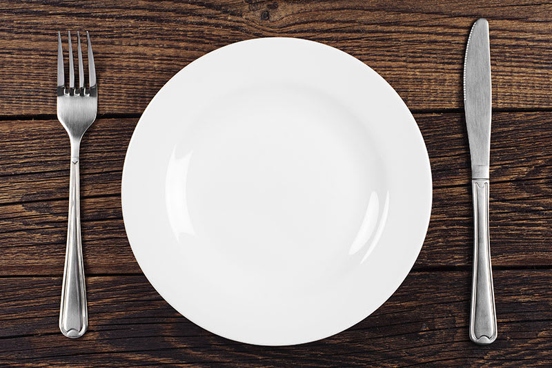 White plate with knife and fork on brown wood table